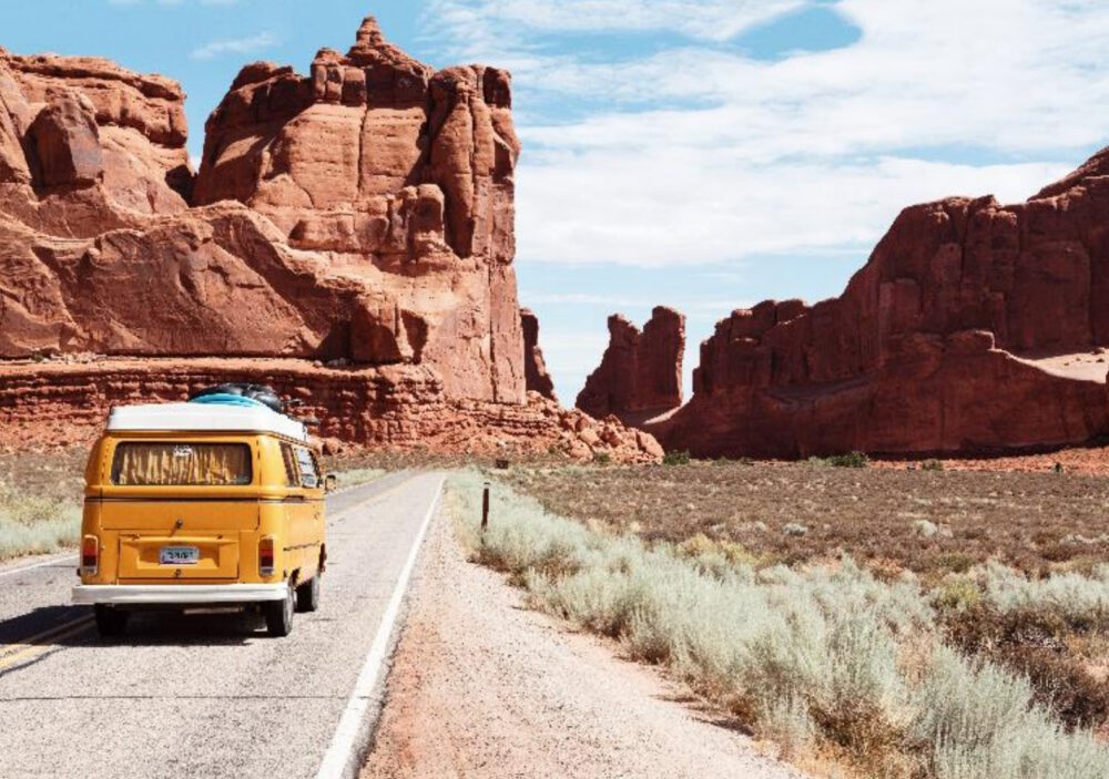 Gelber Volkswagen-Van fährt durch den Arches National Park in Moab, United States.