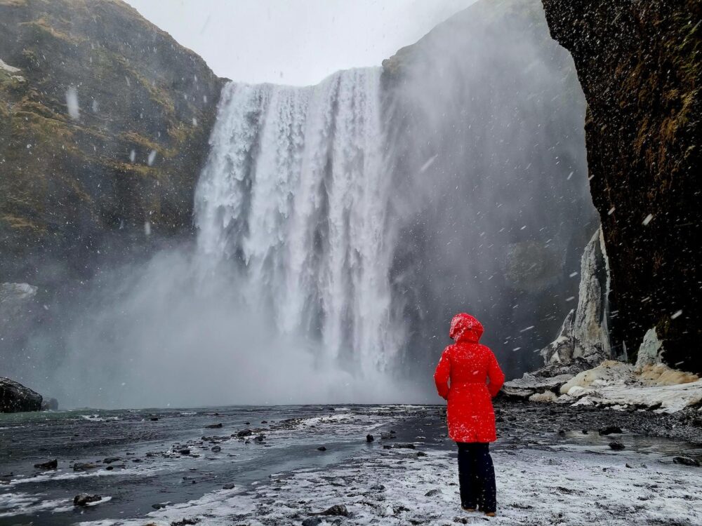 A person in a red coat standing in front of a waterfall