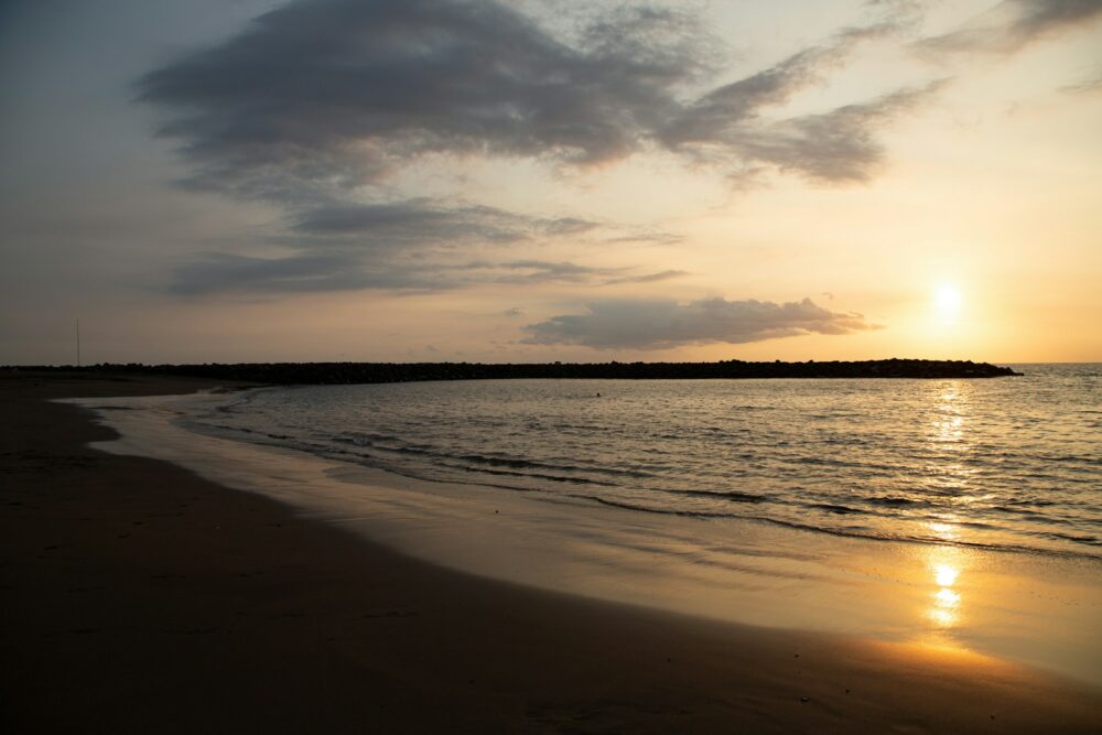 the sun is setting over the water at the beach