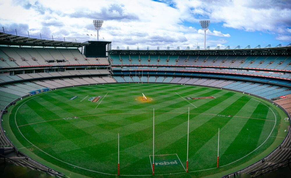 a sports stadium with a field and a field with a crowd of people with Melbourne Cricket Ground in the background